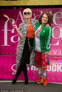 two women standing next to each other in front of a pink wall