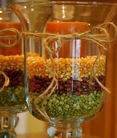 two glass vases filled with corn and carrots on top of a wooden table