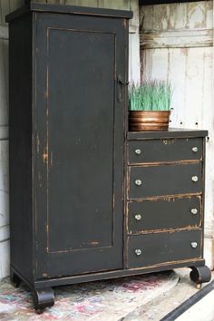 an old black cabinet with a potted plant on it's top and wheels