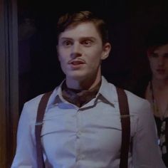 a man with suspenders and a bow tie standing in front of a door, looking at the camera