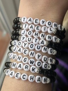 several bracelets with words written in white and black beads on the wrist, all stacked together