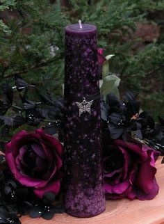 a purple pillar sitting on top of a wooden table next to flowers and greenery