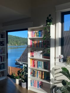 there is a book shelf with many books on it in front of a window overlooking the water