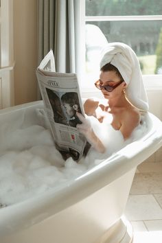 a woman sitting in a bathtub reading a newspaper