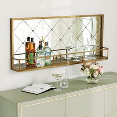 a mirror on the wall above a dresser with bottles and glasses in front of it