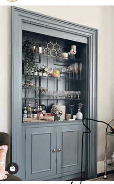 a gray china cabinet with glass doors and shelves filled with vases, candles and other items