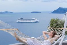 a woman laying in a hammock with a cruise ship in the water behind her