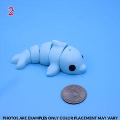 a small white toy laying next to a penny on a blue background with the caption photos are examples only color placement may vary