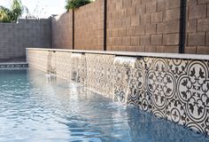 an outdoor swimming pool with tile work on the wall and water running down it's sides