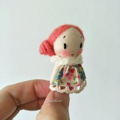 a hand holding a tiny doll with pink hair and dress on it's head