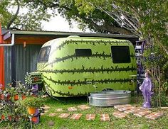 a large green trailer parked next to a tree filled yard with potted plants on it