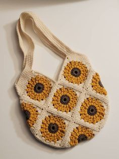 a crocheted bag with yellow flowers on the front and brown centers, hanging from a white wall