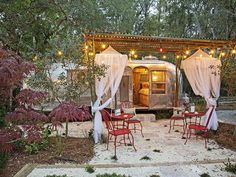 an outdoor dining area with red chairs and lights strung from the roof, next to a trailer