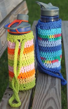 two crocheted water bottles sitting on top of a wooden bench