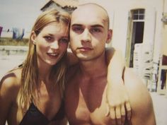 a man and woman posing for a photo on the beach with their arms around each other