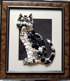 a cat made out of beads and other items in a wooden frame on a wall