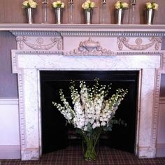 a vase filled with white flowers sitting in front of a fire place