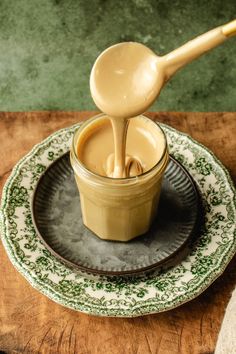 a wooden spoon pouring liquid into a bowl on top of a green and white plate