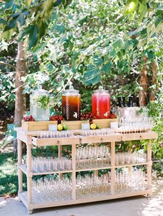 an outdoor bar with glasses, lemons and drinks on the table in front of some trees