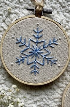 two embroidered snowflakes are sitting on a table next to some flowers and scissors