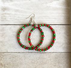 two red and green beaded hoop earrings sitting on top of a white wooden table