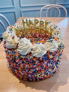 a birthday cake with white frosting and sprinkles on it sitting on top of a wooden table