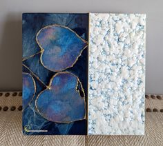 two pieces of art sitting on top of a table next to each other, one is blue and the other is white