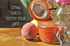 small batch stone fruit jam in a glass jar next to two peaches on a wooden table