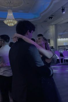 a man and woman dance together in a ballroom with chandelier hanging from the ceiling