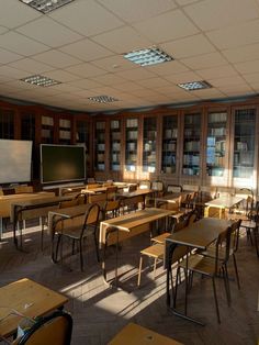 an empty classroom with wooden desks and bookshelves in front of large windows