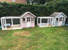 three different colored dog houses sitting in the middle of a yard with grass and bushes behind them