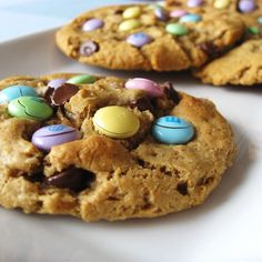 three cookies with m & m's and chocolate chips on them sitting on a white plate