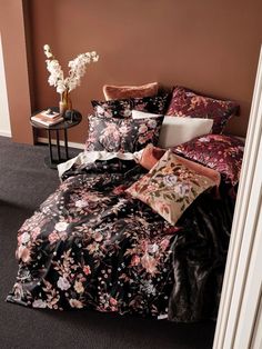 a bed covered in black and pink floral comforter next to a vase with white flowers