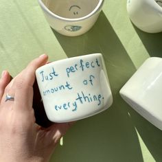 a person holding a ceramic mug with writing on it next to other cups and bowls