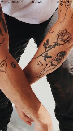 two people with tattoos on their arms holding each other's hands and looking down at the ground