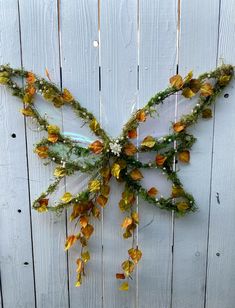 a butterfly made out of leaves and flowers on a wooden fence with string attached to it