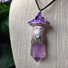 a purple necklace with a mushroom on it and a green bead hanging from the back