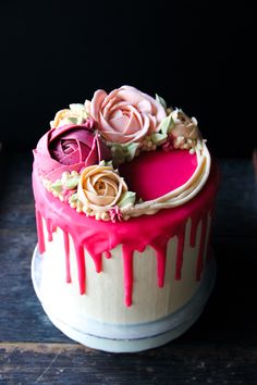 a cake with pink icing and flowers on top is sitting on a wooden table