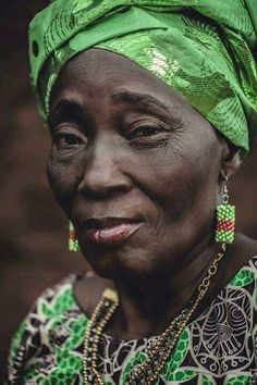 an older woman wearing a green headdress and smiling at the camera with her eyes wide open