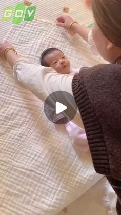 a baby laying on top of a bed next to a woman holding her hand out