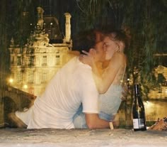 a man and woman kissing while sitting next to each other with a bottle of wine in front of them