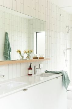 a bathroom with white tile and green towels on the shelf above the bathtub is also decorated with flowers