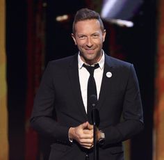 a man in a black suit and tie holding a microphone at an awards ceremony or show