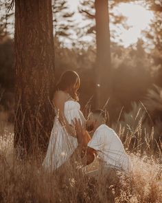 two people sitting in the grass next to each other near a tree and some tall grass