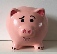 a pink pig with black spots on it's eyes and nose, sitting on a shelf