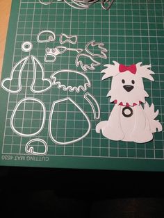 a cutting board with scissors and paper cut outs on it, including a dog wearing a red bow