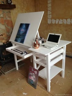 a laptop computer sitting on top of a white desk next to a painting easel