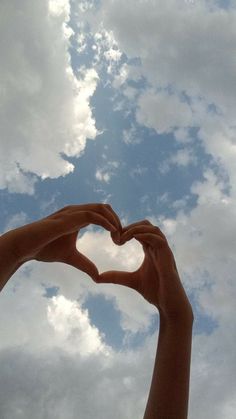 two hands in the shape of a heart against a cloudy sky