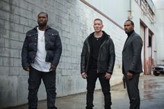 three men standing next to each other in front of a building