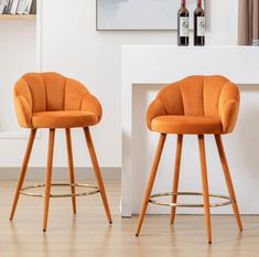 two orange chairs sitting next to each other in front of a white fireplace with wine bottles on the mantel